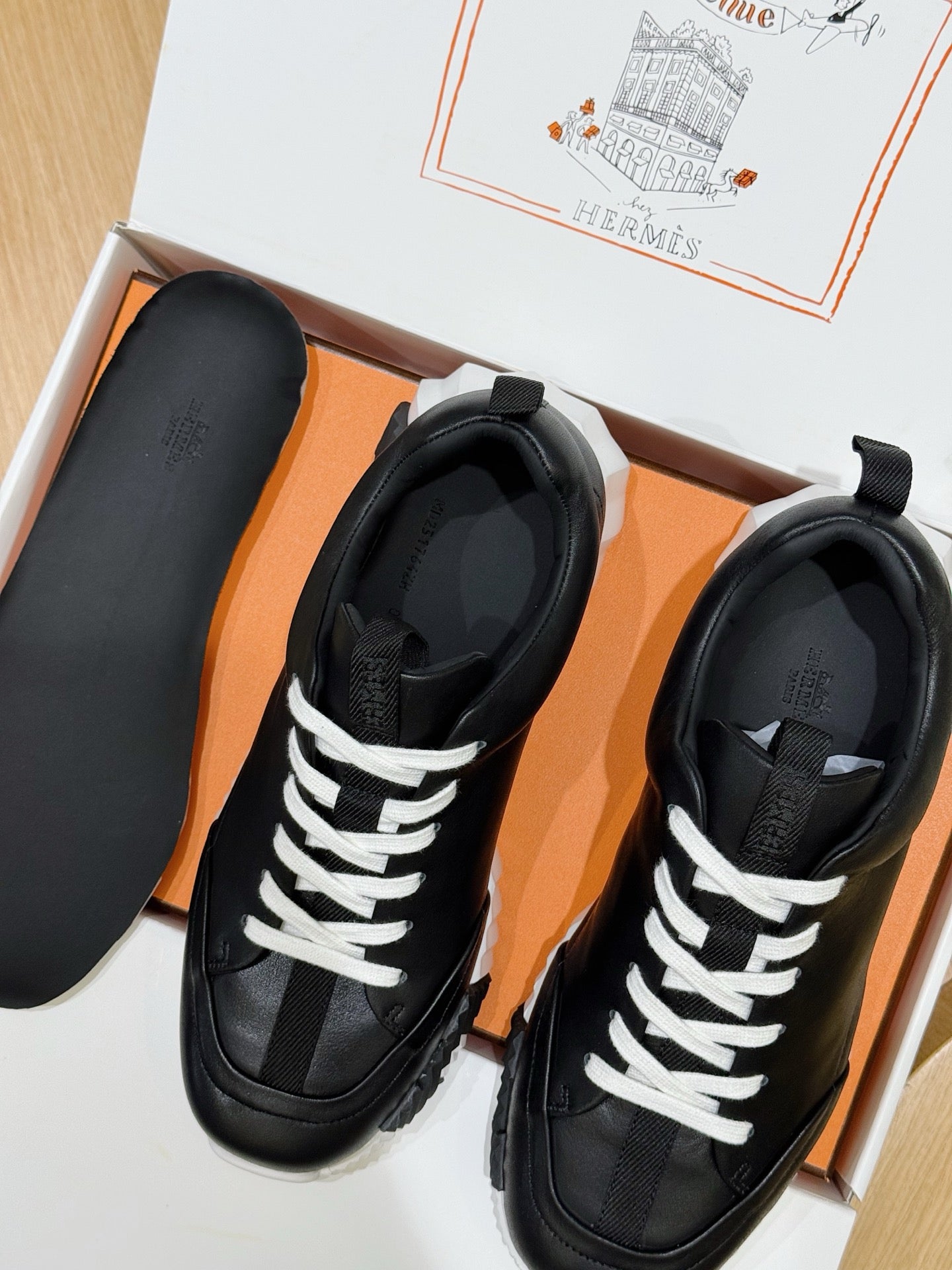 Two black lace-up sneakers with white laces in orange shoe box