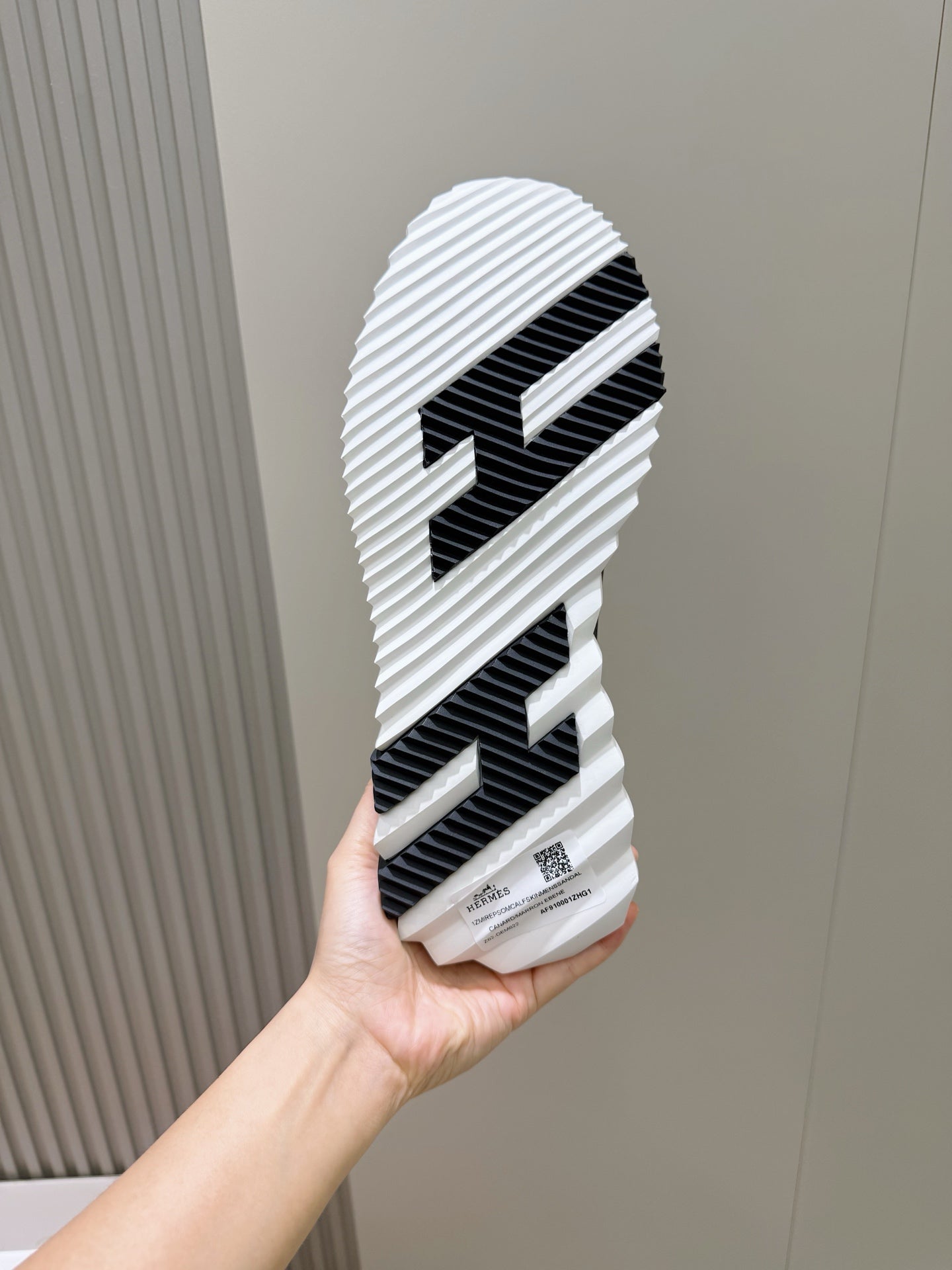 Black and white sneaker outsole with striped tread, held in hand