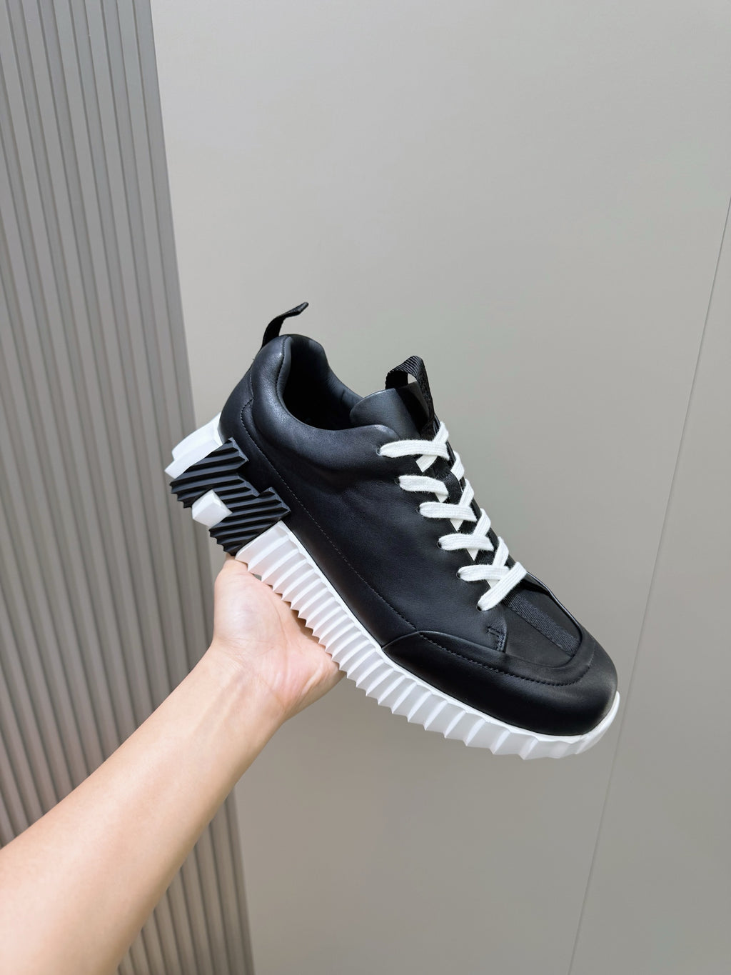 Black lace-up sneaker held in hand with white laces and platform sole