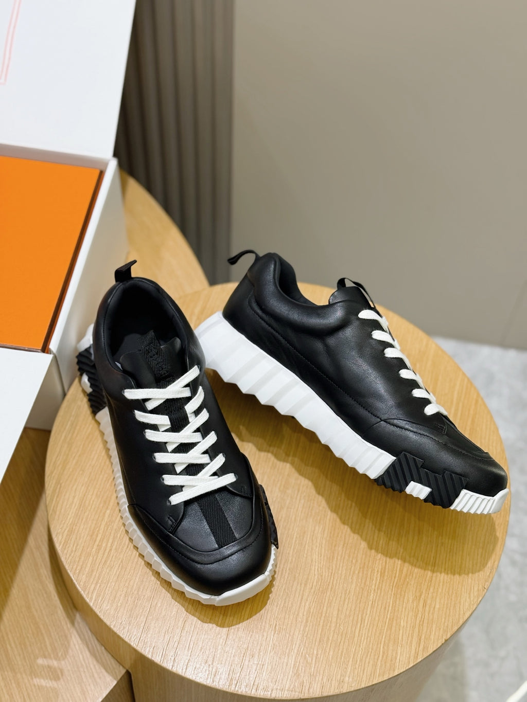 Pair of black lace-up sneakers with white laces on round wooden display