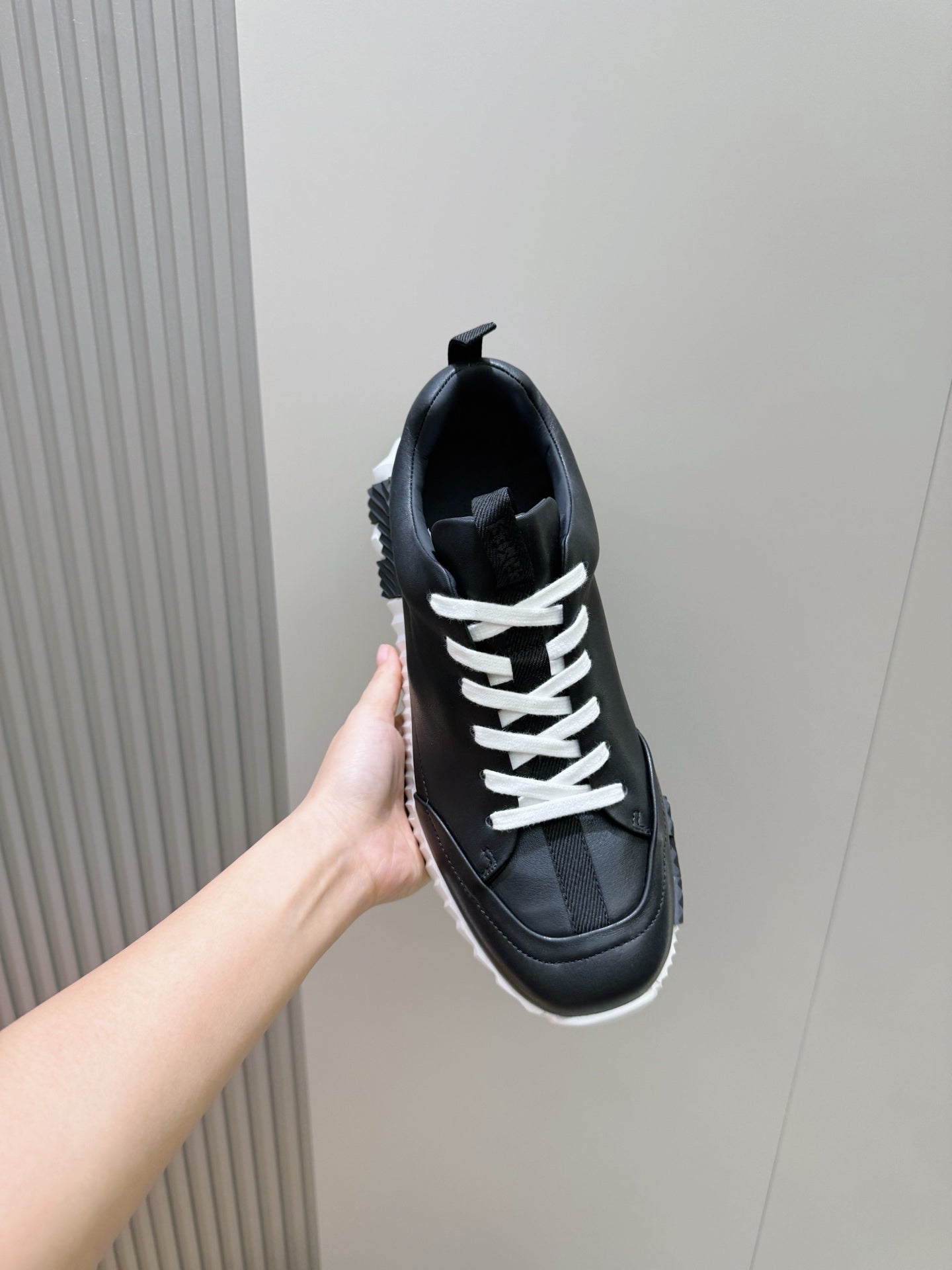 Hand holding black lace-up sneaker with white laces and chunky sole