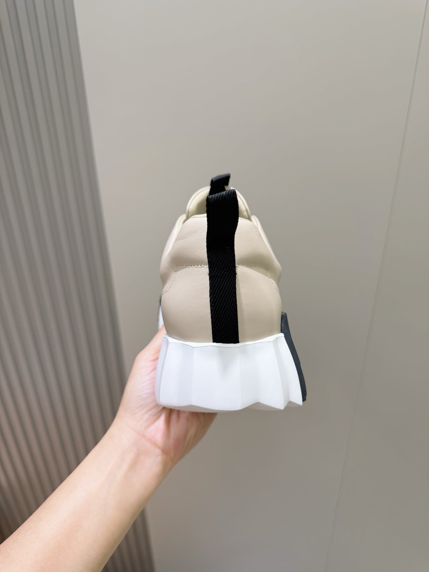 Unisex luxury sneaker by Hermes, cream back view with black heel strap and tab