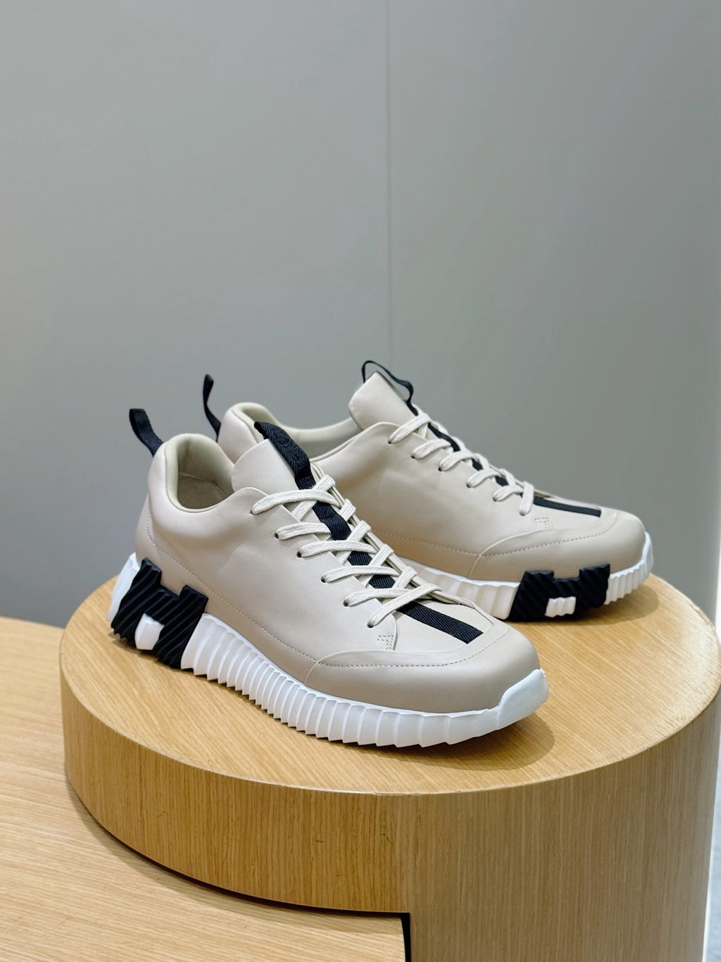 Hermes unisex sneakers on a stand, light cream leather with black side detailing