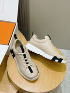 Hermes unisex sneakers shown side by side, light cream with black side stripes