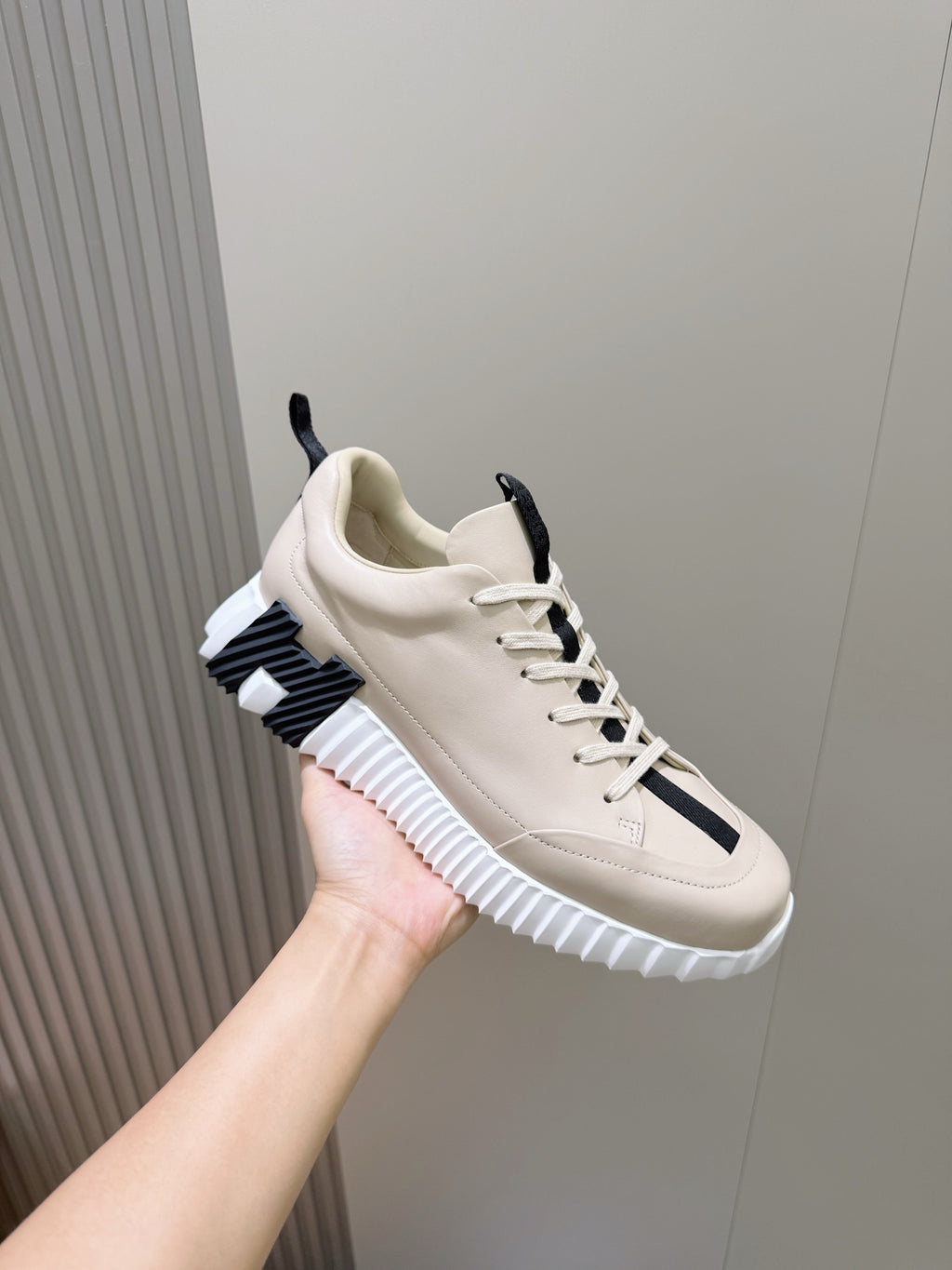 Unisex luxury sneaker by Hermes, cream upper with navy side panel, lace-up with chunky sole