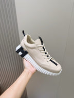 Hermes unisex sneaker held up, light cream with black stripe panel and white sole