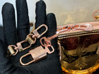 Louis Vuitton bag close-up with multiple key rings and front hardware over pink metallic body.