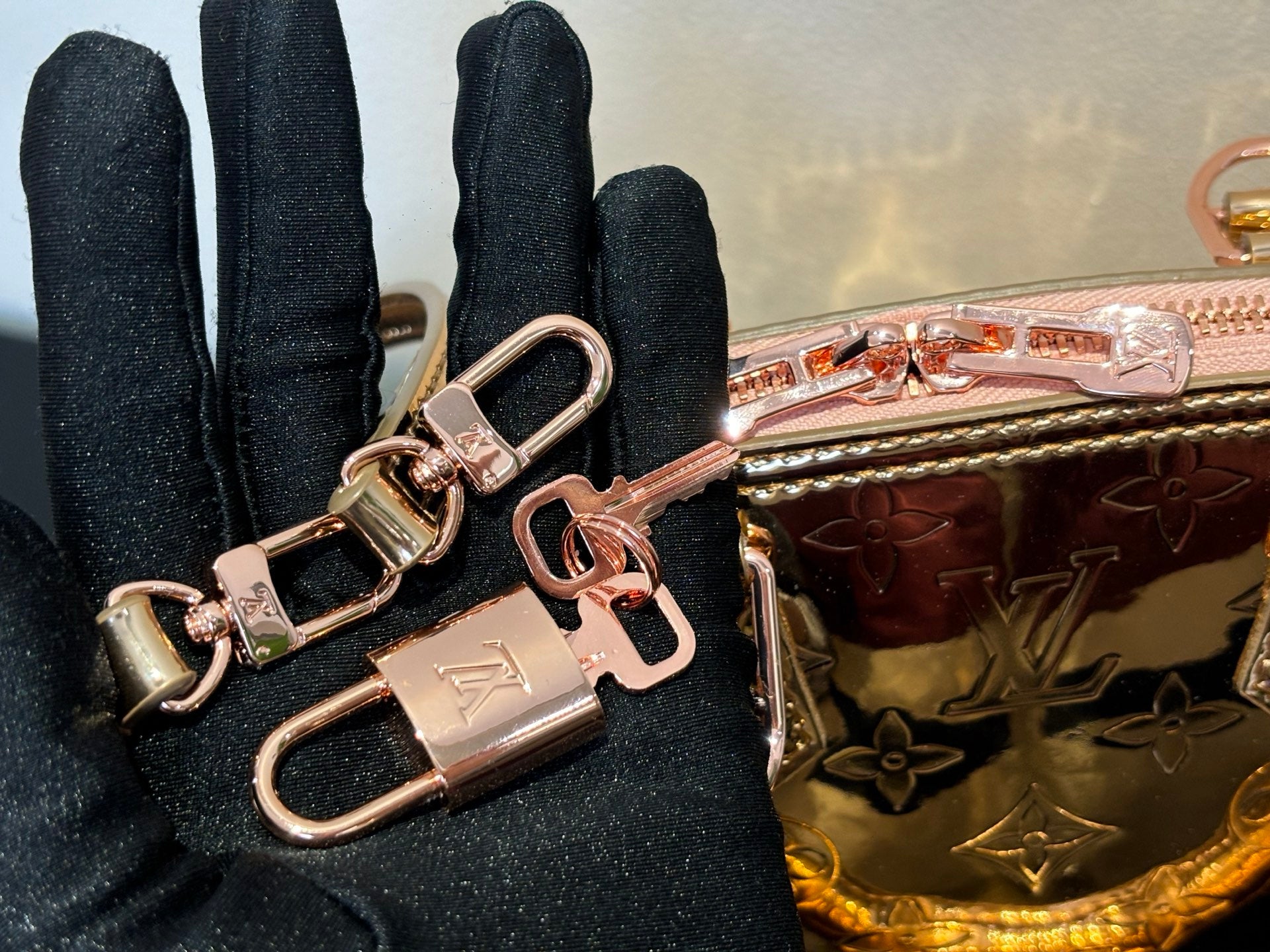 Louis Vuitton bag close-up with multiple key rings and front hardware over pink metallic body.