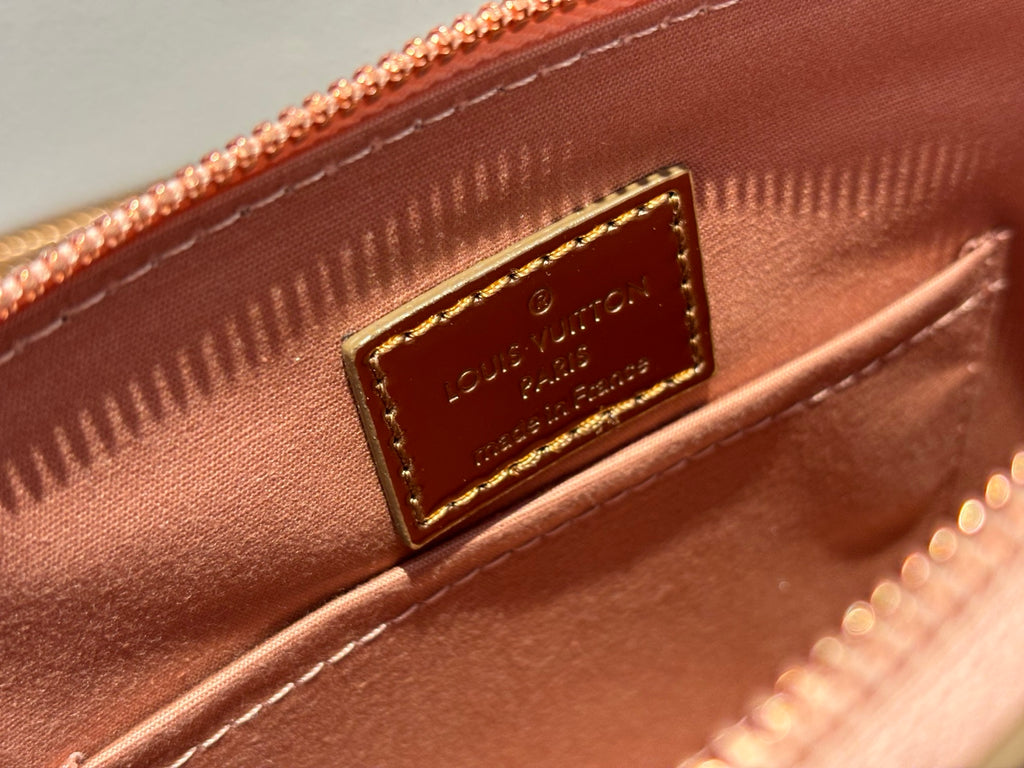 Louis Vuitton bag interior tag close-up on pink lining, gold embossed label and stitching.