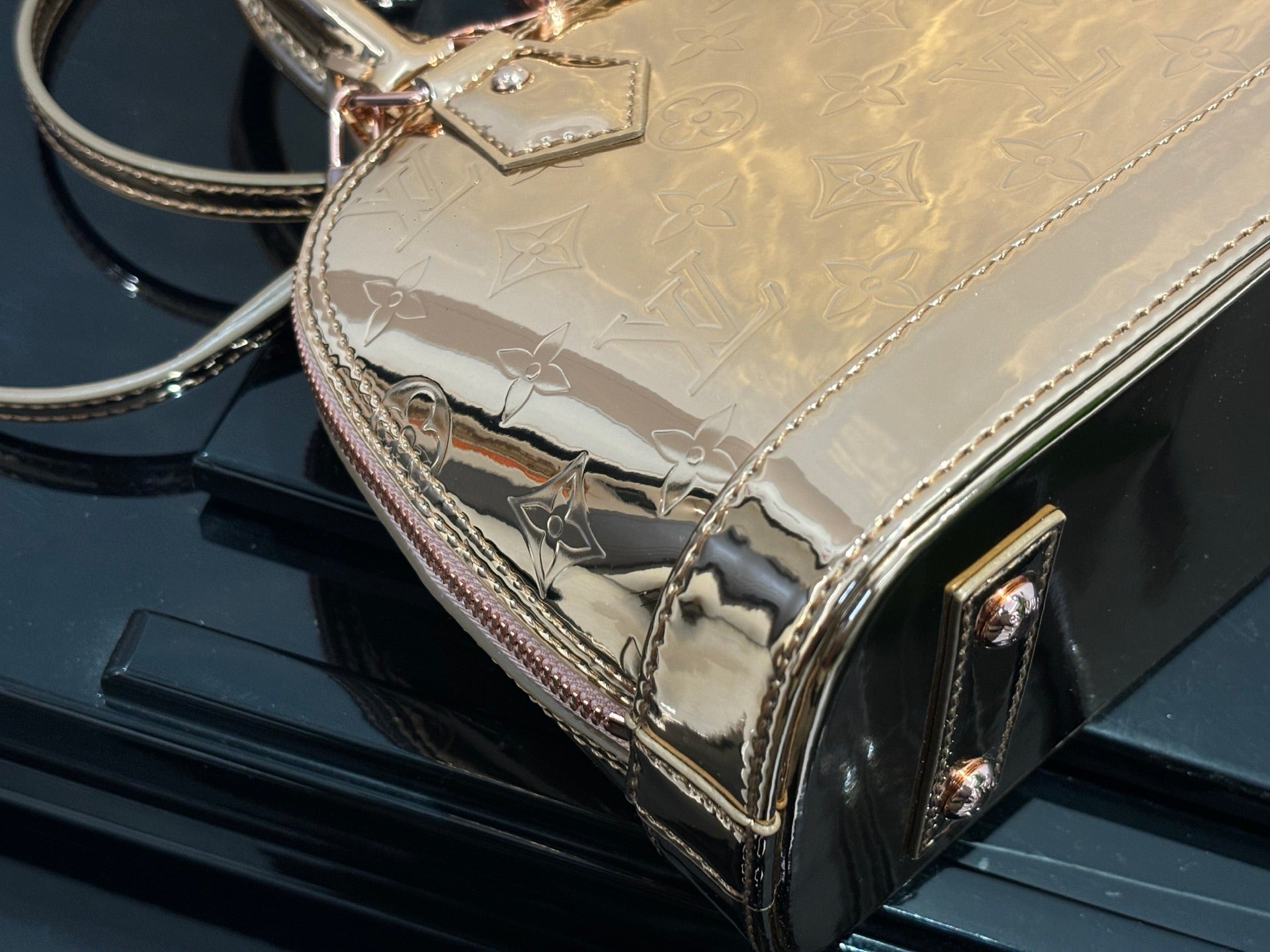 Louis Vuitton bag detail with gold embossed monogram, pink edging, and front corner hardware.