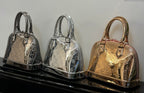 Louis Vuitton bags trio on display: silver and gold metallic monogram with top handles.