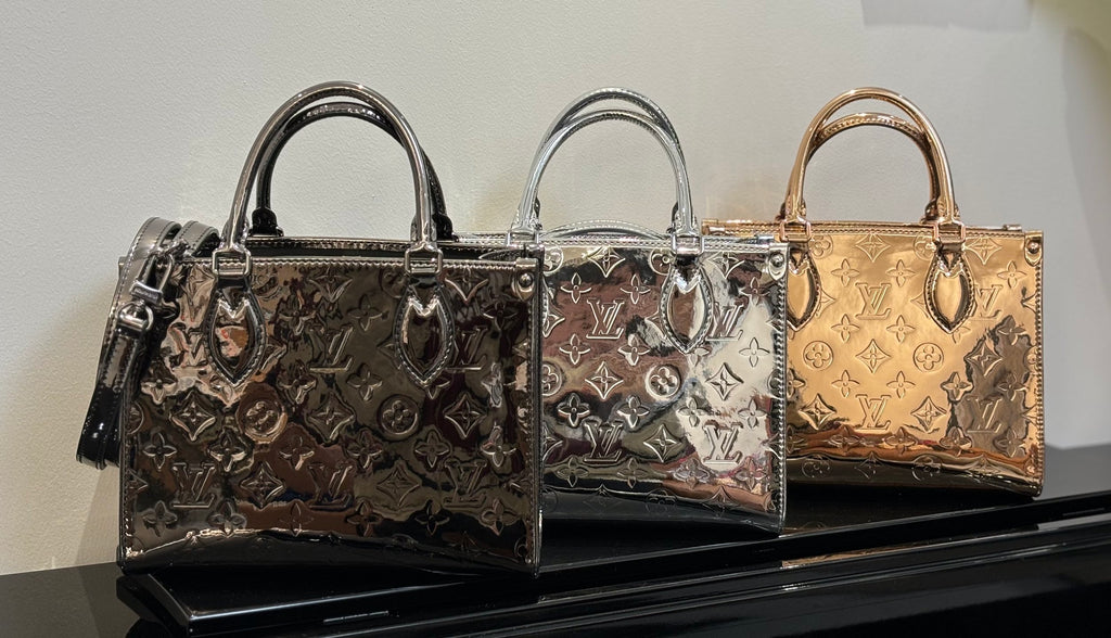 Louis Vuitton handbags lineup on display, three patterned styles with top handles and shoulder straps