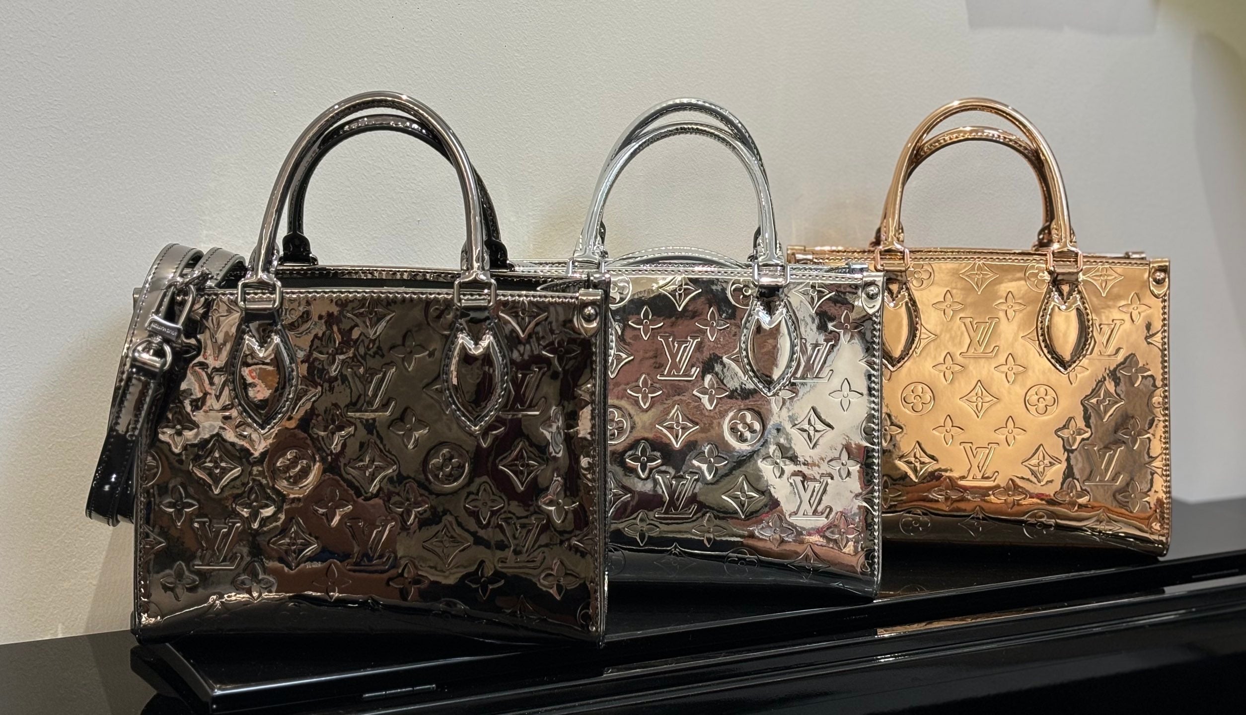 Louis Vuitton handbags lineup on display, three patterned styles with top handles and shoulder straps