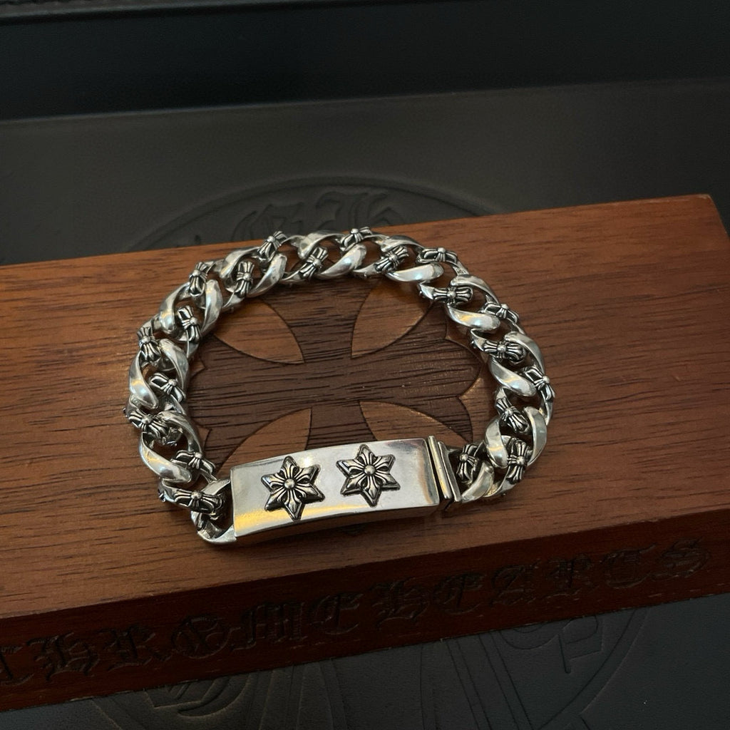 Silver-toned chain bracelet on wooden surface, rectangular center clasp with two cross-flower emblems
