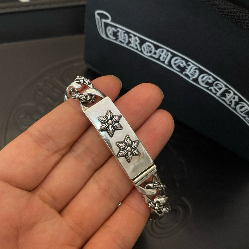 Silver-toned chain bracelet on hand, rectangular center tag with two cross-flower emblems