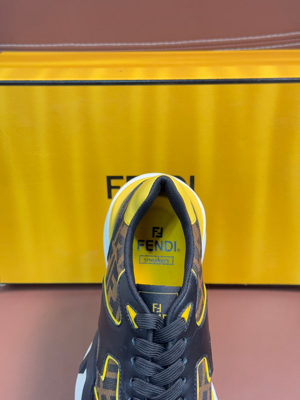 Fendi unisex sneaker close-up at toe, dark FF upper with yellow accents and lace-up front.