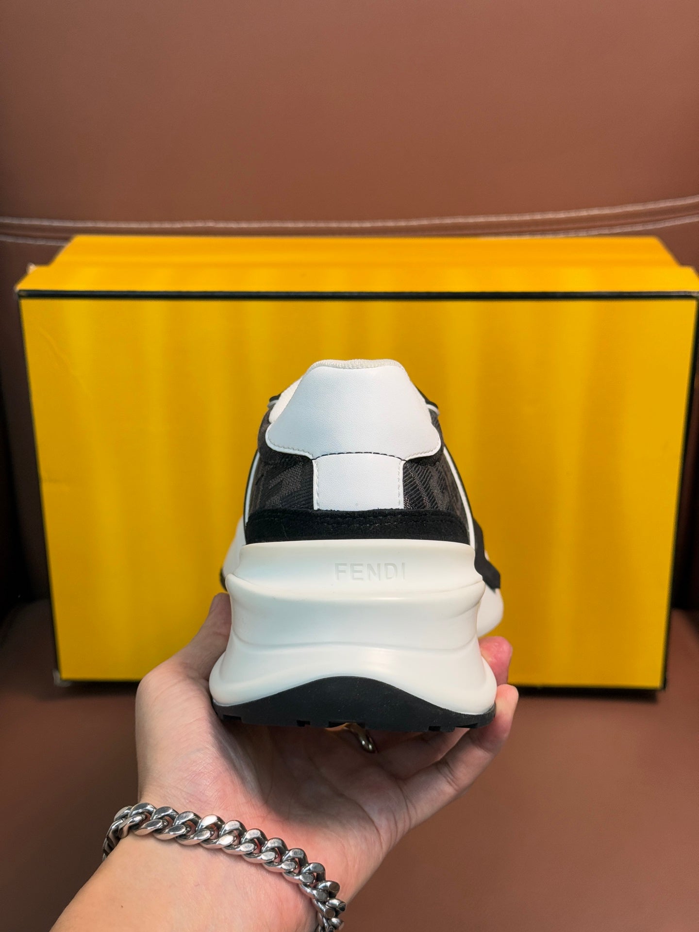 Hand holding Fendi unisex sneaker heel, black upper with white heel cap and sole.
