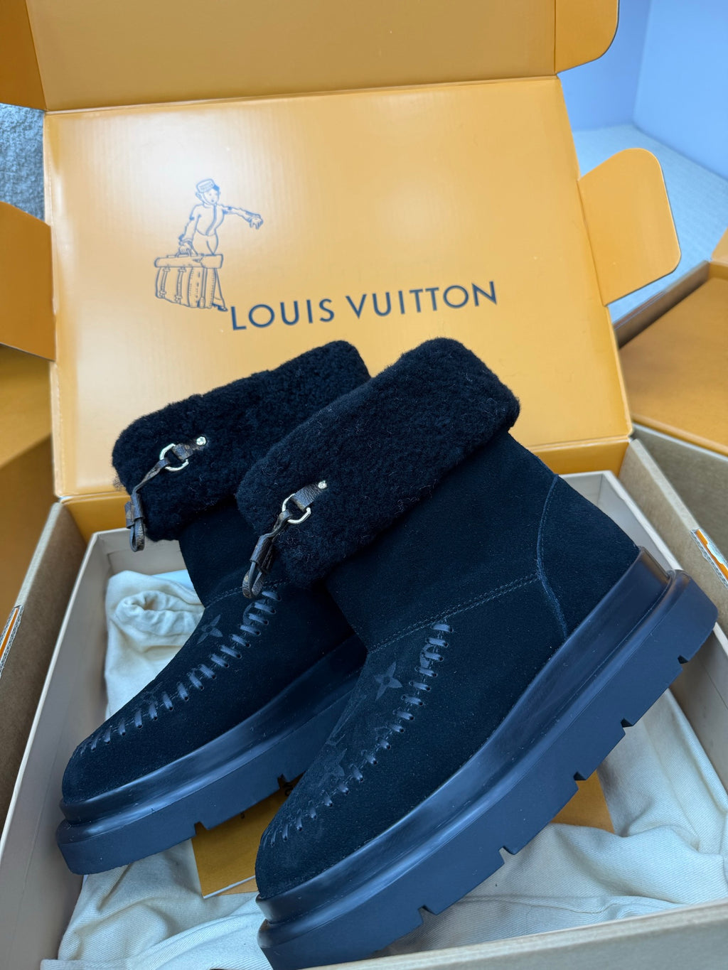 Dark navy Louis Vuitton high-top boots with shearling cuffs, buckle straps, and monogram print