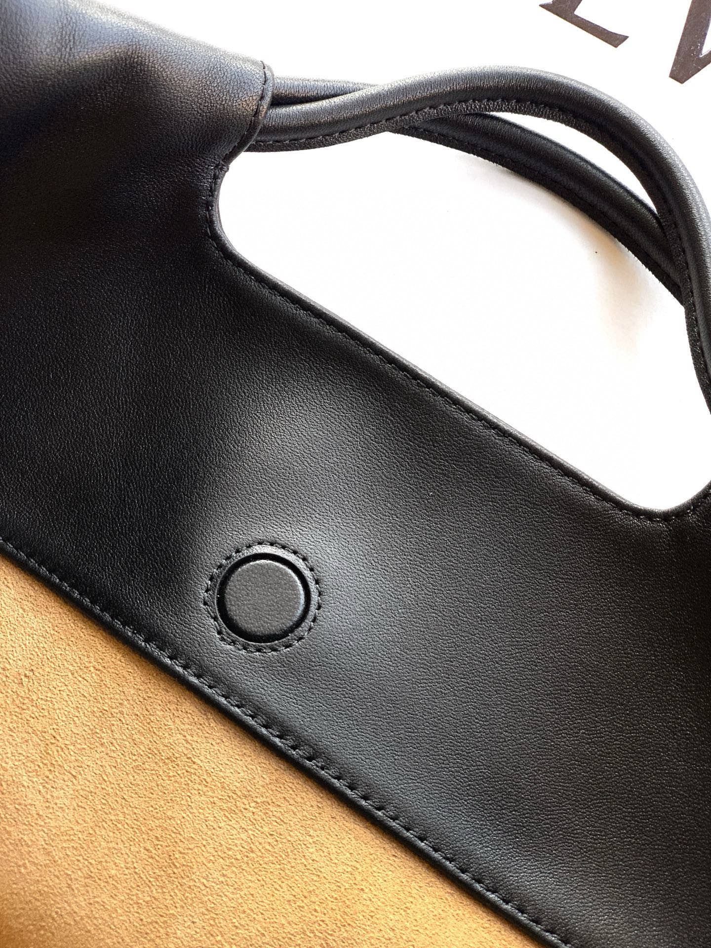 Loewe bag detail: black leather strap with circular grommet and stitched edge