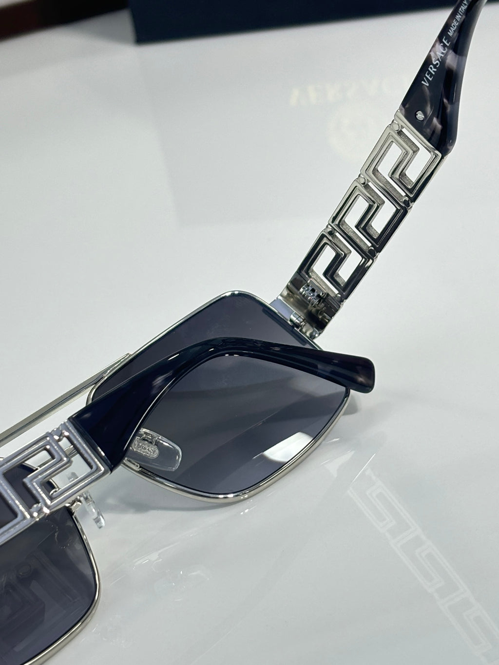 Sunglasses temple close-up with metal Greek key inlays and dark lens front
