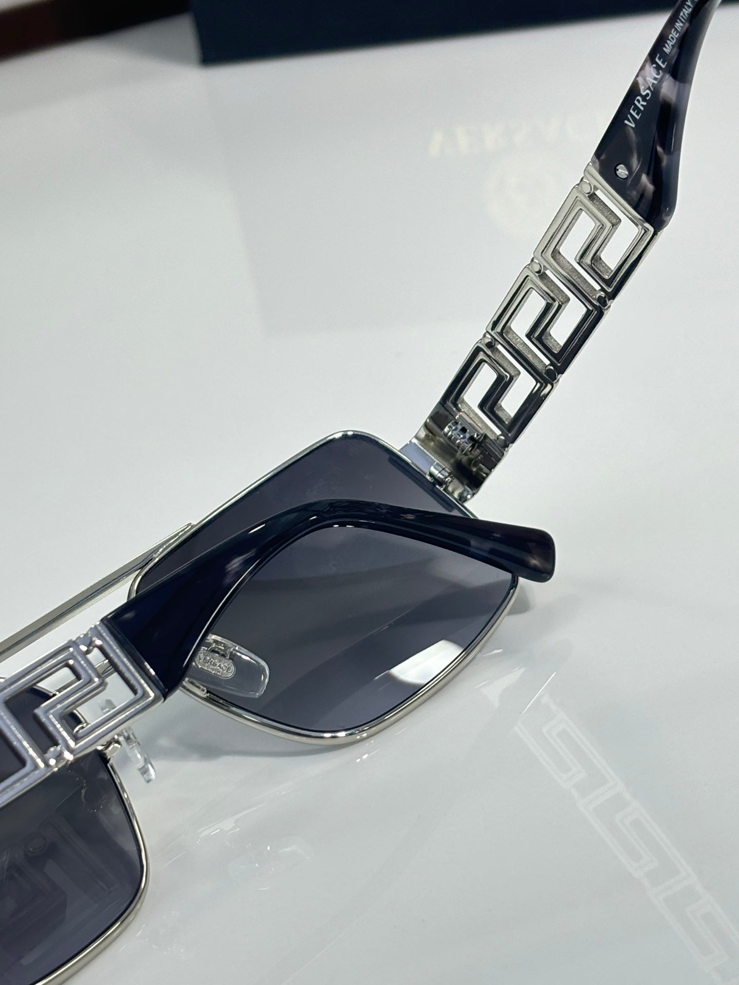 Sunglasses temple close-up with metal Greek key inlays and dark lens front