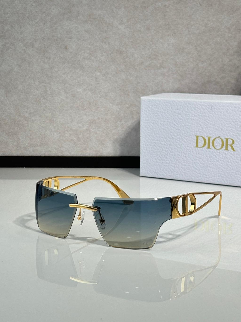 Dior sunglasses with gold frame and blue gradient lenses, front three-quarter view.