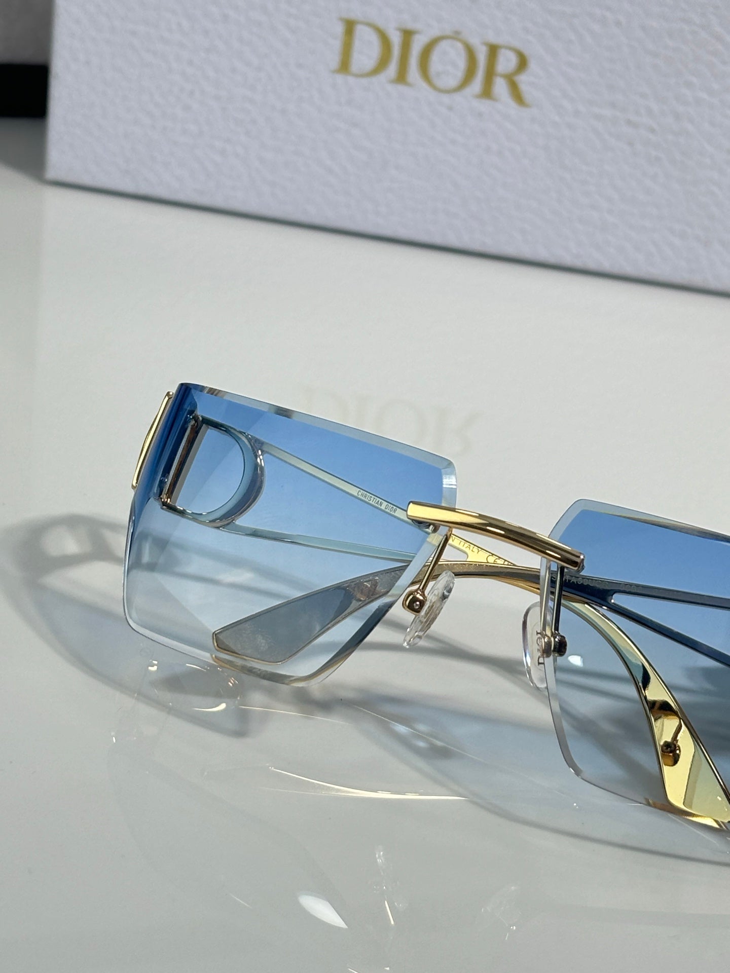 Dior sunglasses close-up showing blue lenses and gold temple with hinge detail.