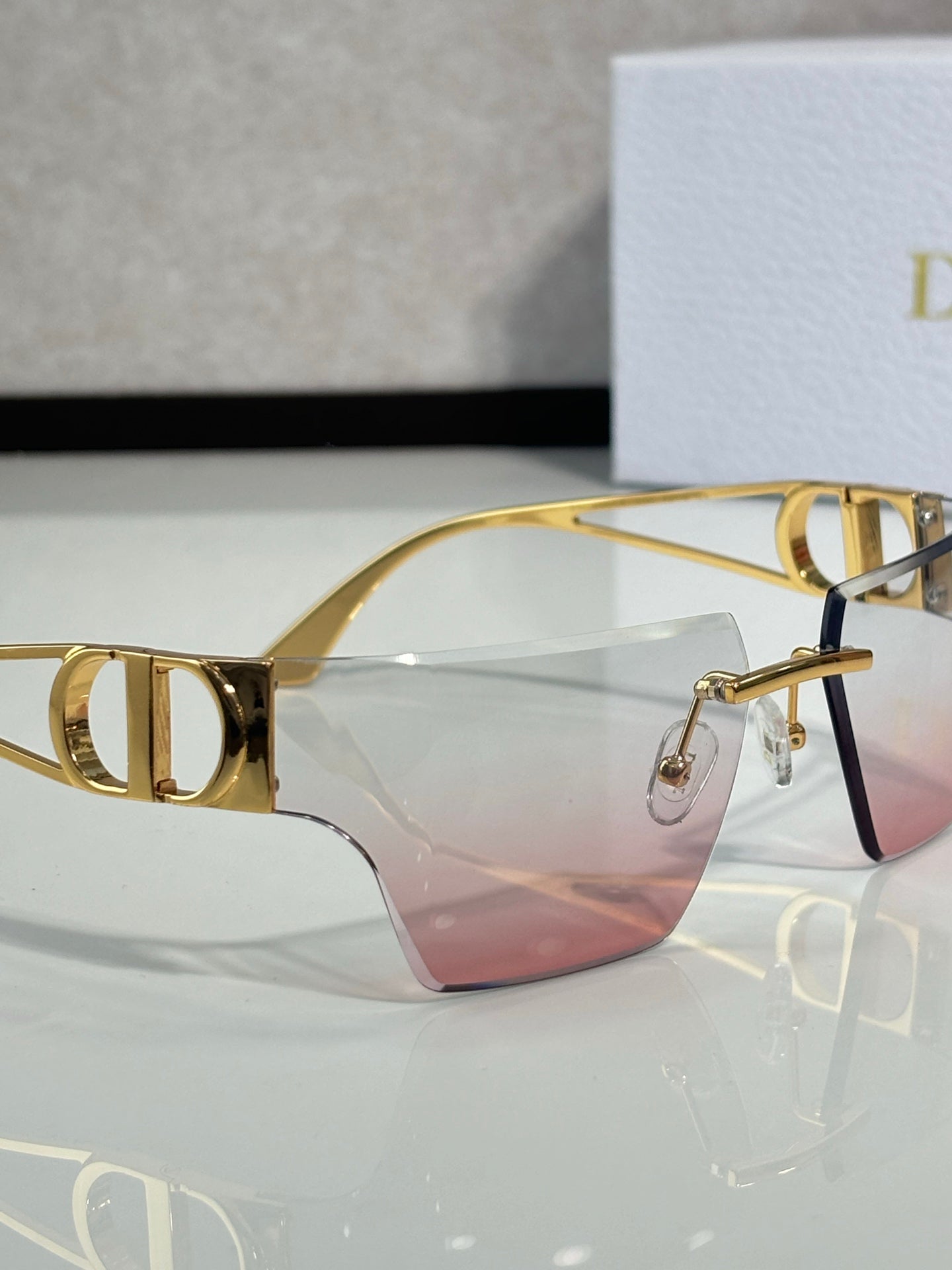 Dior sunglasses close-up of gold frame and pink gradient lenses, front view.