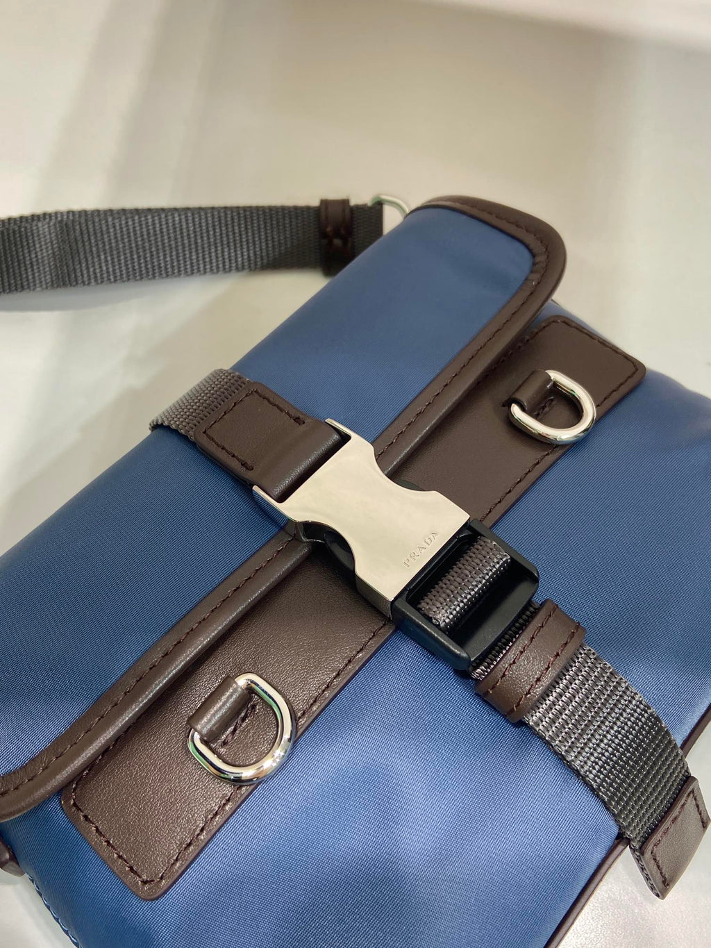 Close-up of blue bag strap with brown buckle hardware and metal D-rings