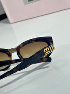 Cat-eye sunglasses close-up, gold “miu miu” logo on temple, tinted lens
