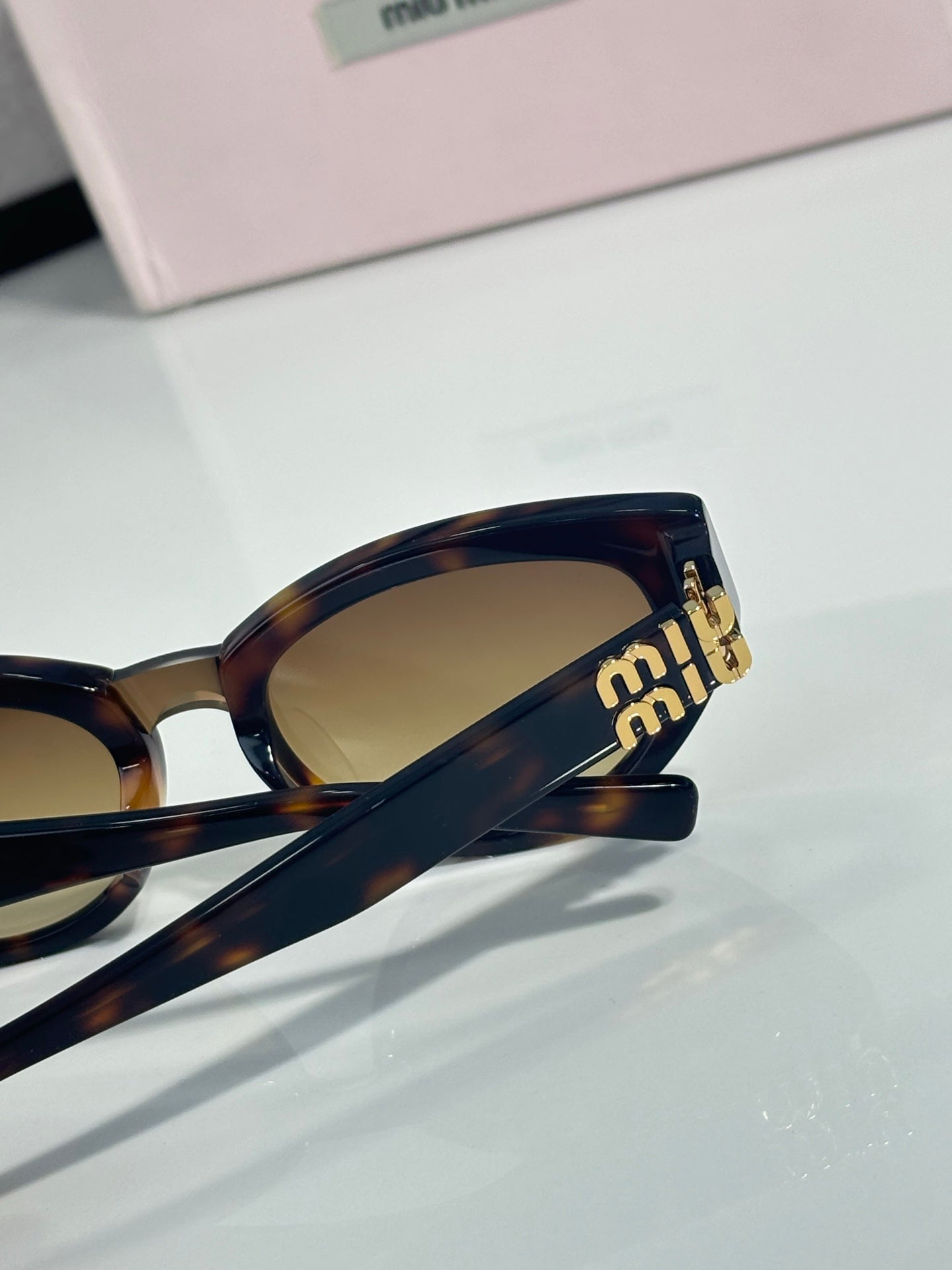Cat-eye sunglasses close-up, gold “miu miu” logo on temple, tinted lens