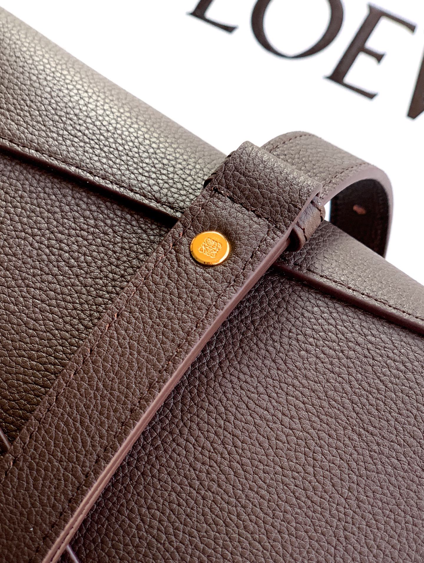 Dark brown leather bag corner with round gold-tone stud detail and folded strap