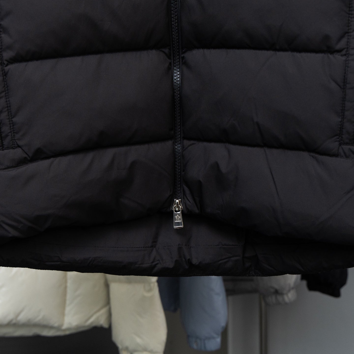 Black long puffer jacket front with centered zipper and quilted horizontal panels