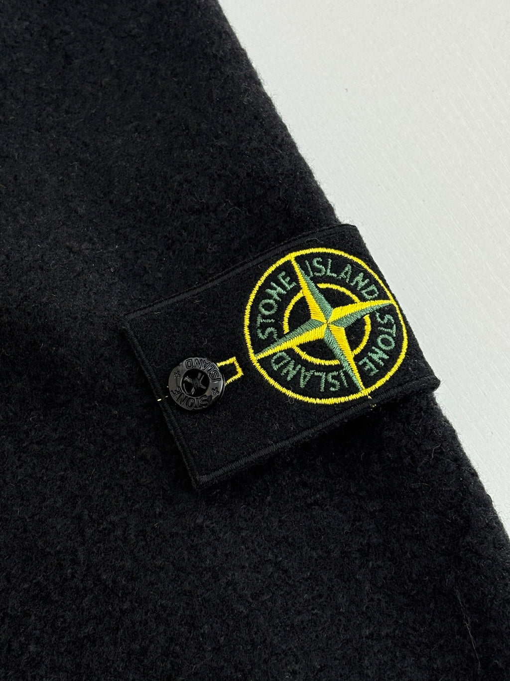Dark jacket sleeve with Stone Island logo patch and button detail