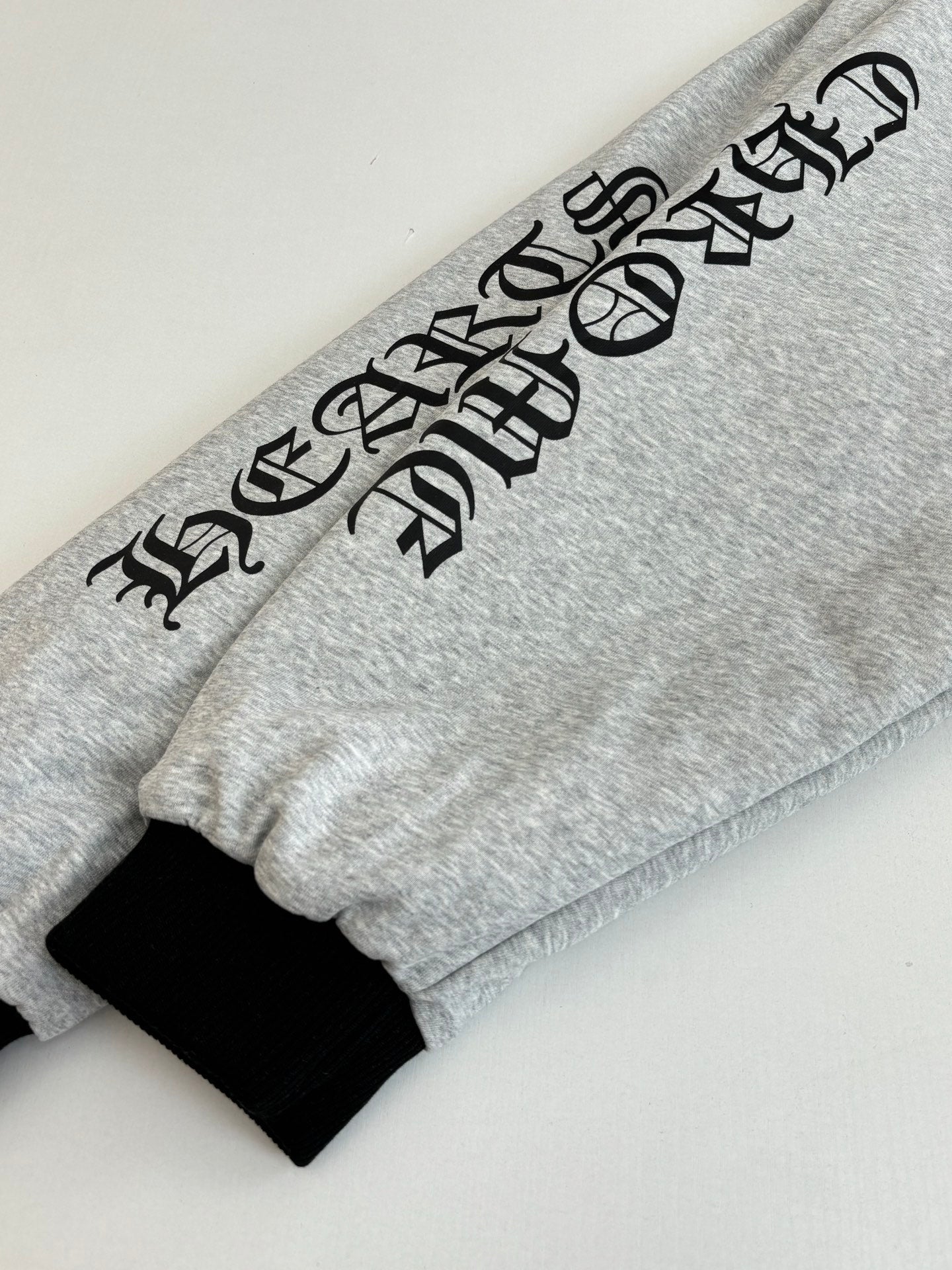 Gray hoodie sleeve with black graphic lettering and black cuff