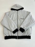 Heather gray zip-up hoodie with hood and small chest emblem, black ribbed cuffs
