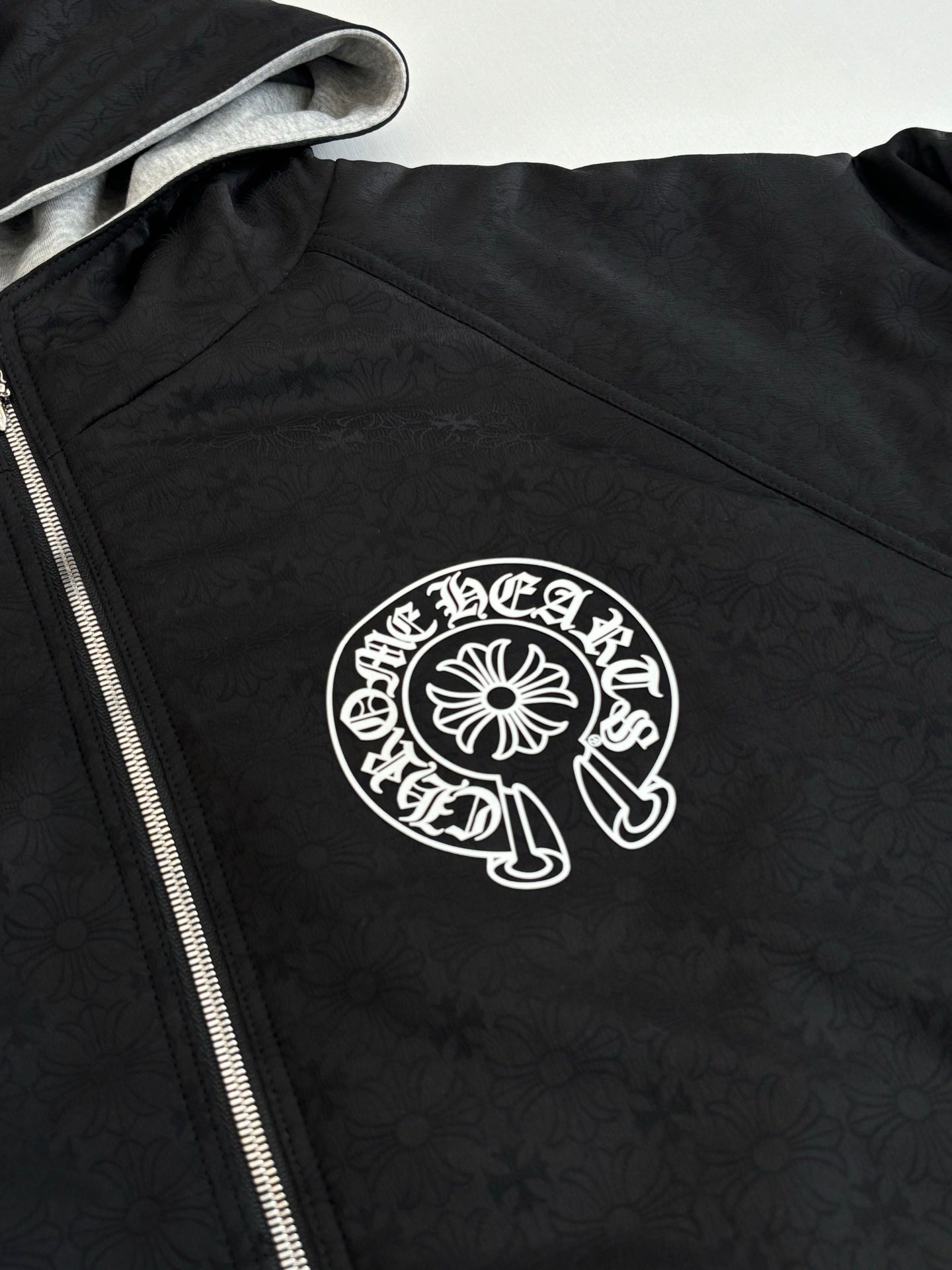 Black zip-up hoodie with hood and white circular chest logo on textured fabric
