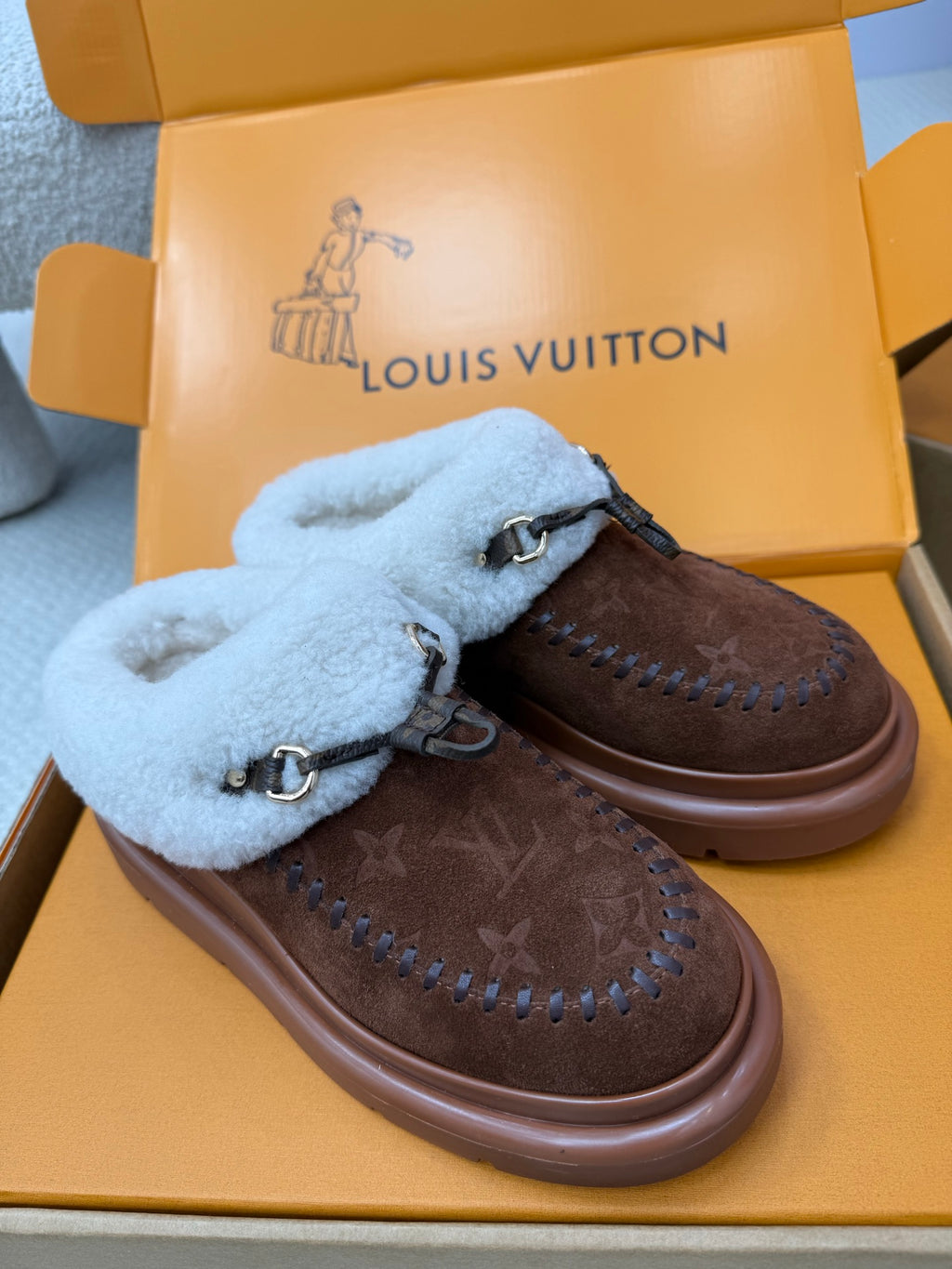 Louis Vuitton shearling mules, side view of brown monogram uppers and blue fur trim