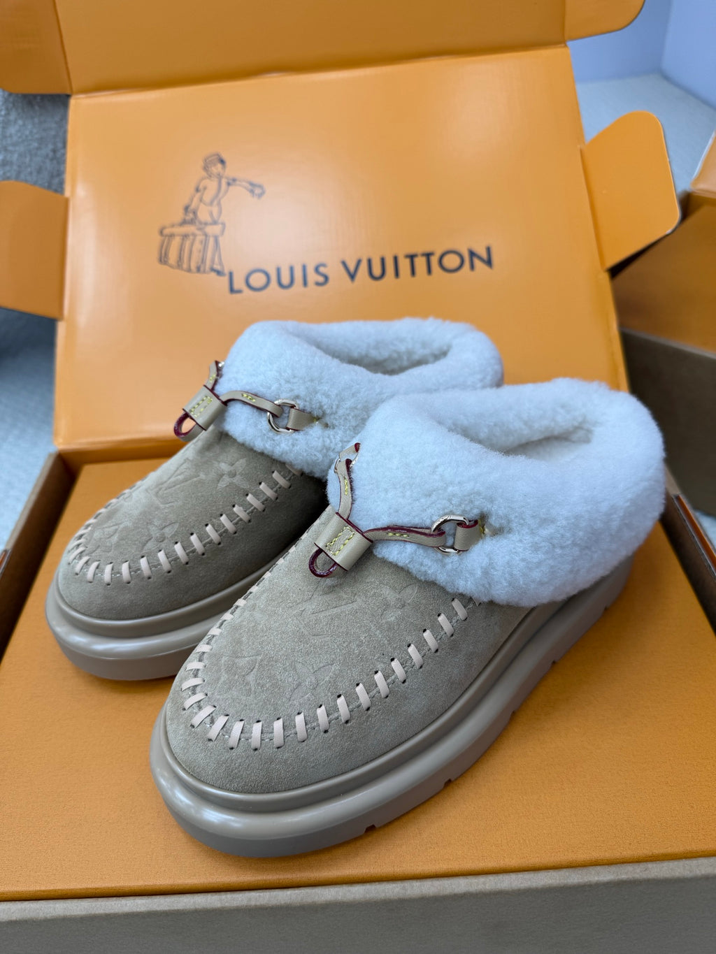 Pair of grey suede slip-on sneakers with light blue fur lining and metal buckle straps