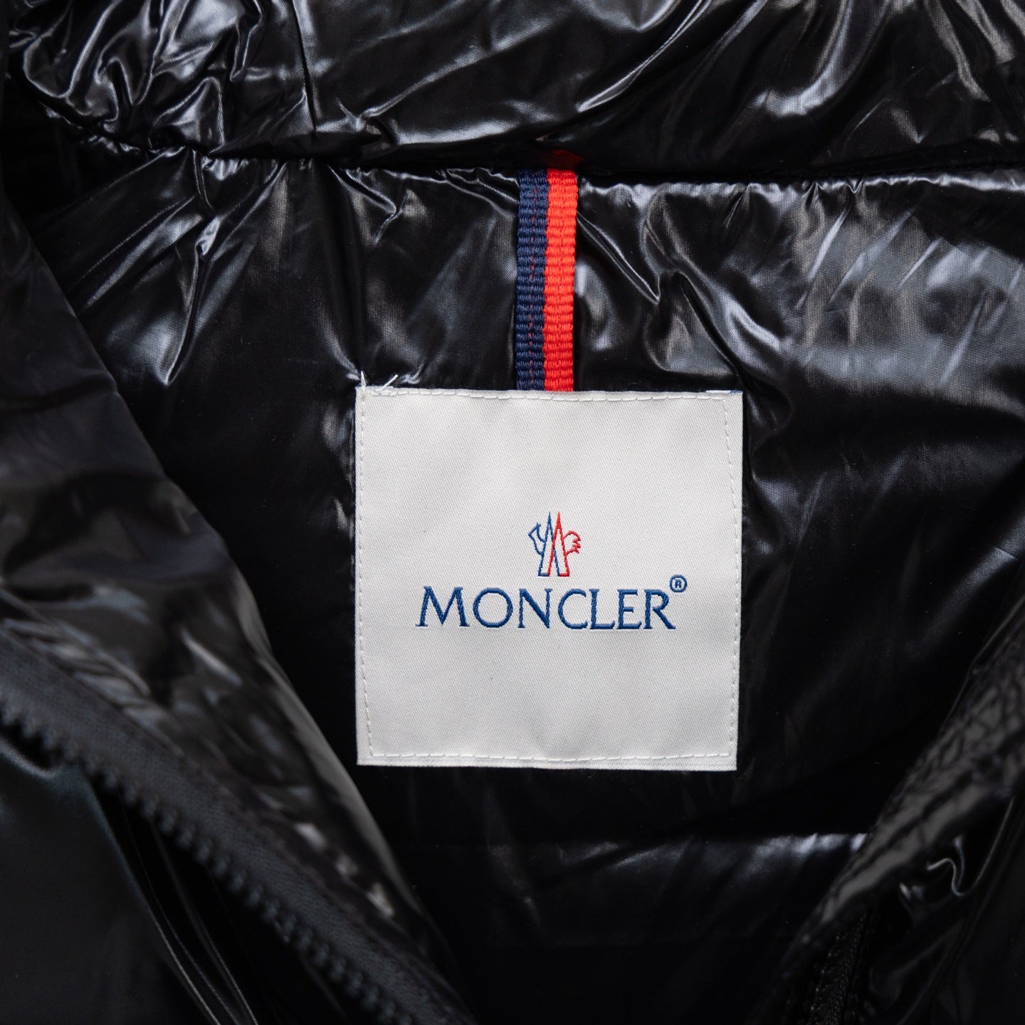 Moncler logo patch on black puffer jacket collar, with blue-red stripe trim