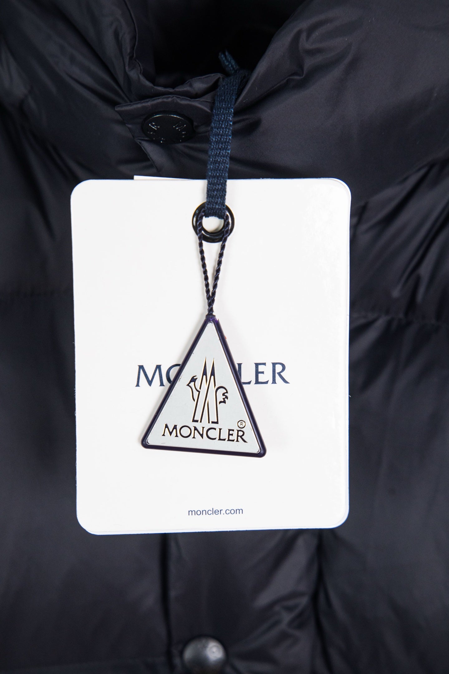 Moncler long puffer jacket with brand swing tag hanging from the hood opening