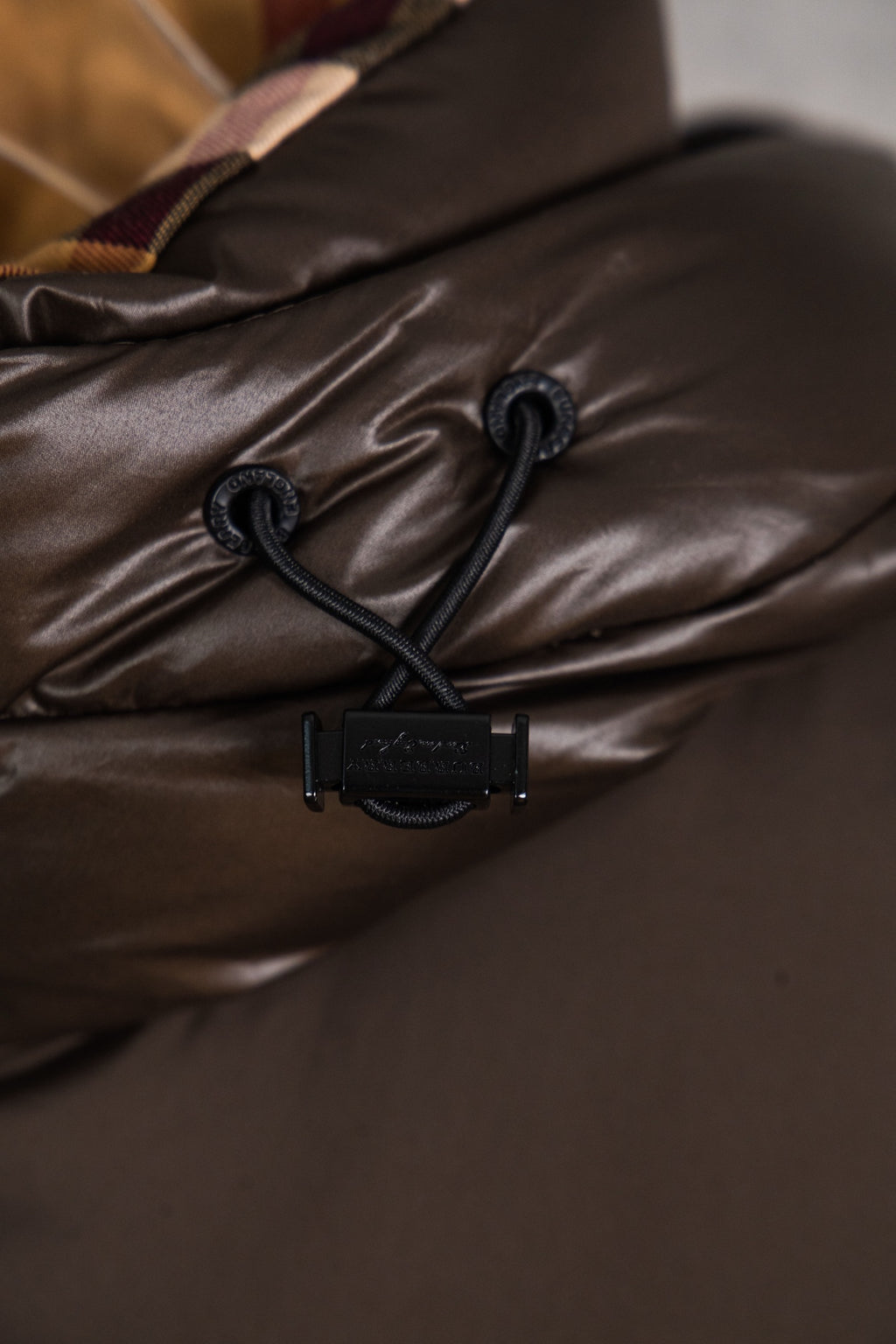Long puffer jacket hood cinch with black cord and toggles on dark brown fabric