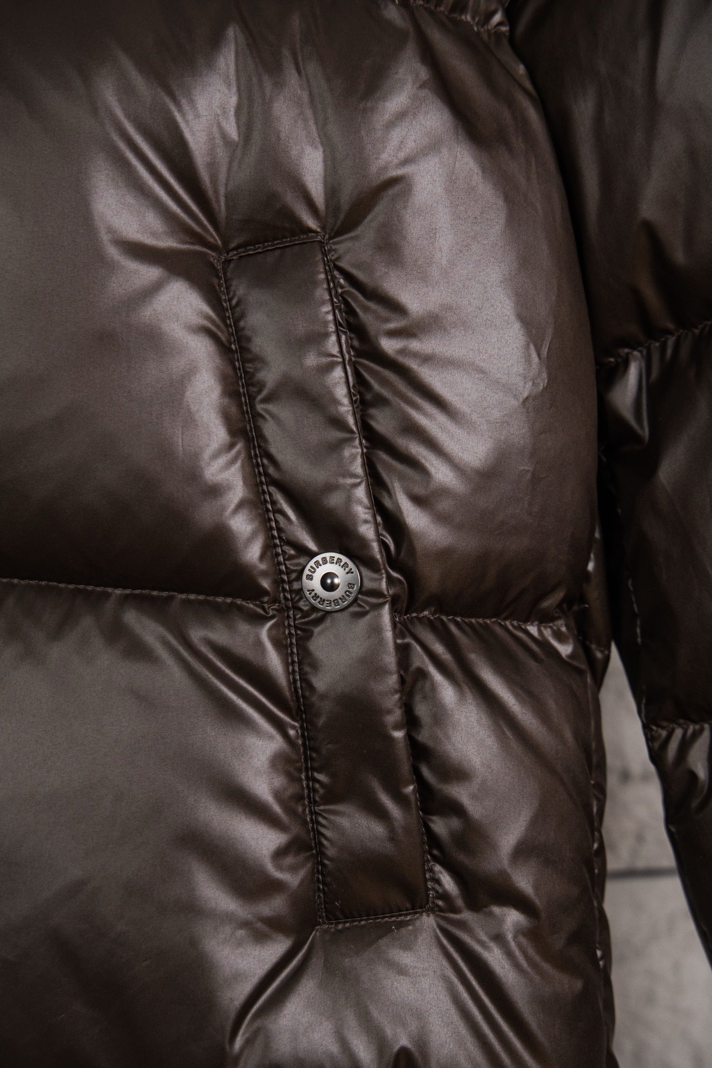 Long puffer jacket upper front with round snap button on dark brown quilting