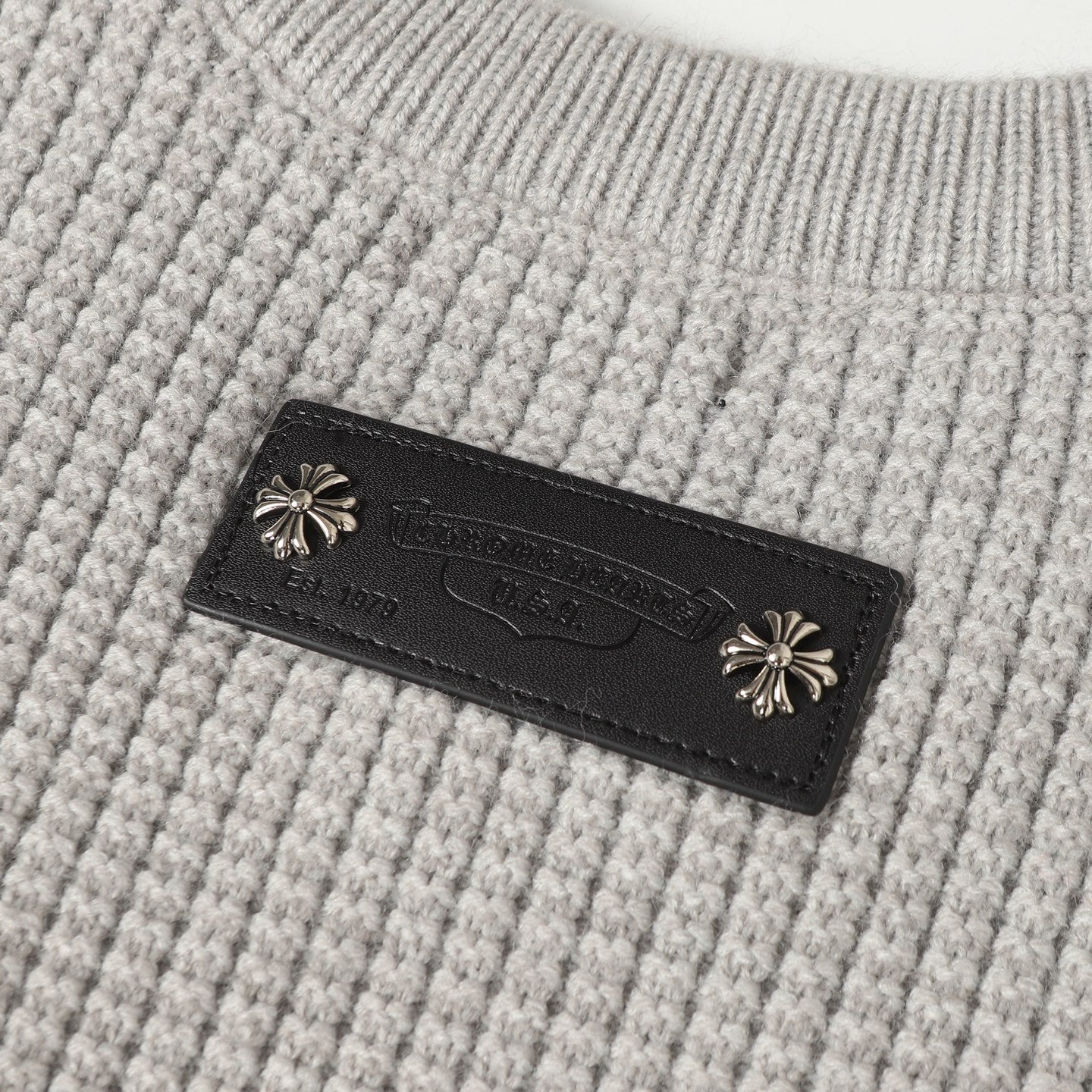 Light gray knit fabric with dark leather brand label and decorative studs