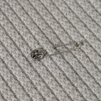 Light gray knit fabric with small metal pin ornament on ribbed texture