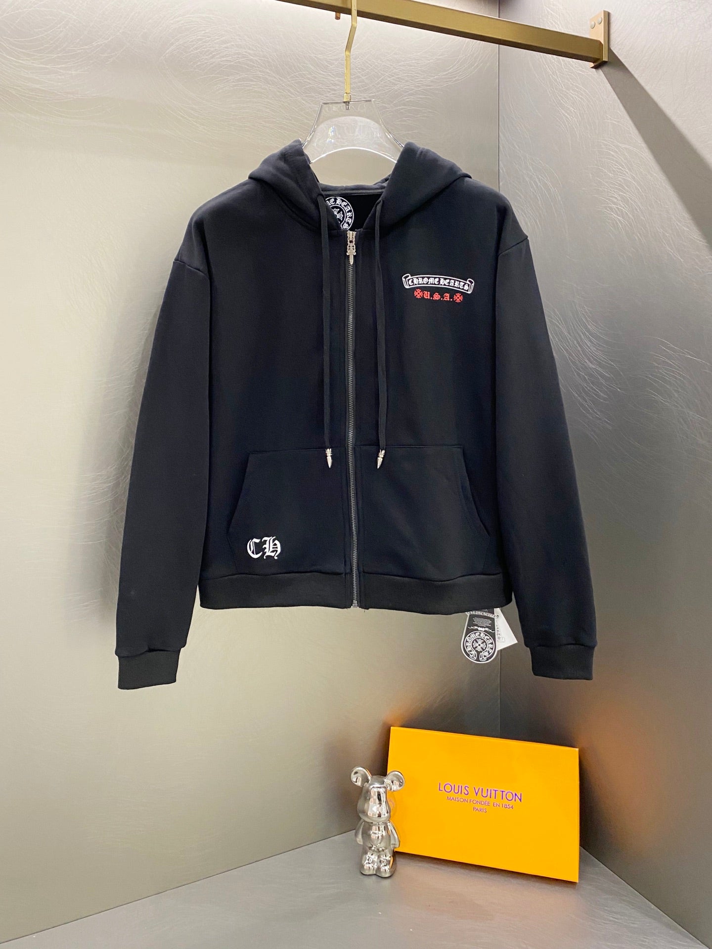 Dark zip-up hoodie with hood, front pockets, and small chest patch logo