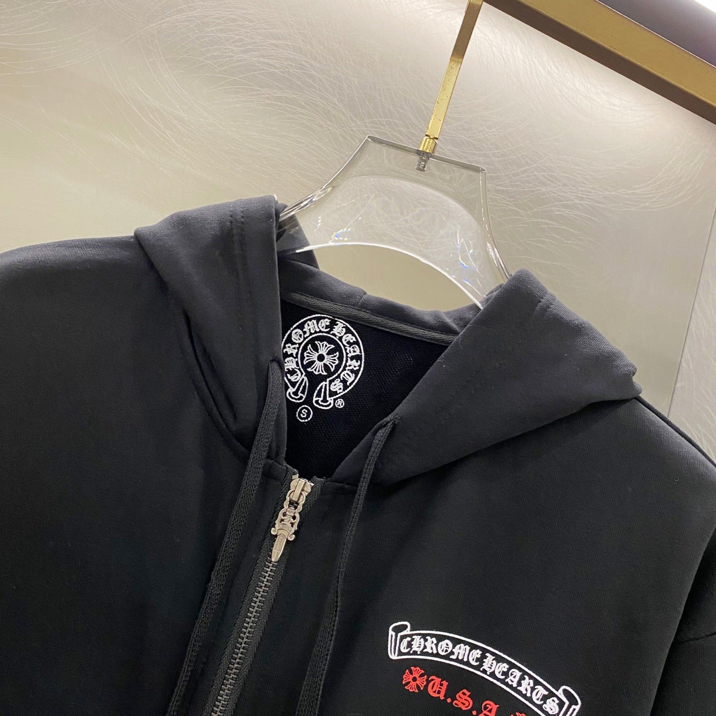 Dark hoodie close-up showing hood lining, front zipper, and chest logo patch