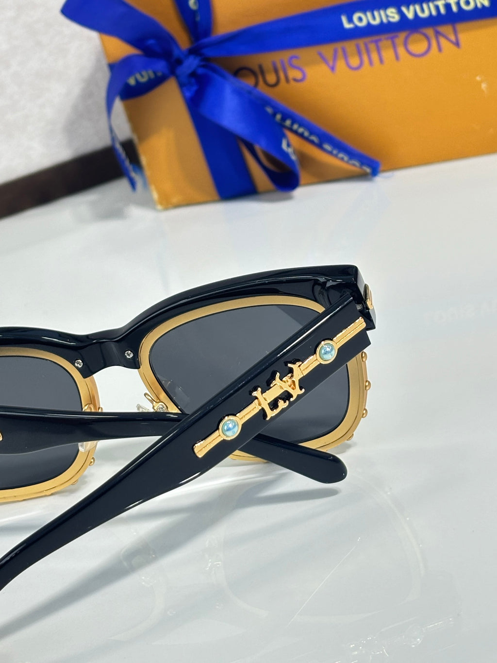Louis Vuitton sunglasses, side view: gold emblem on black frame, blue-tinted lenses