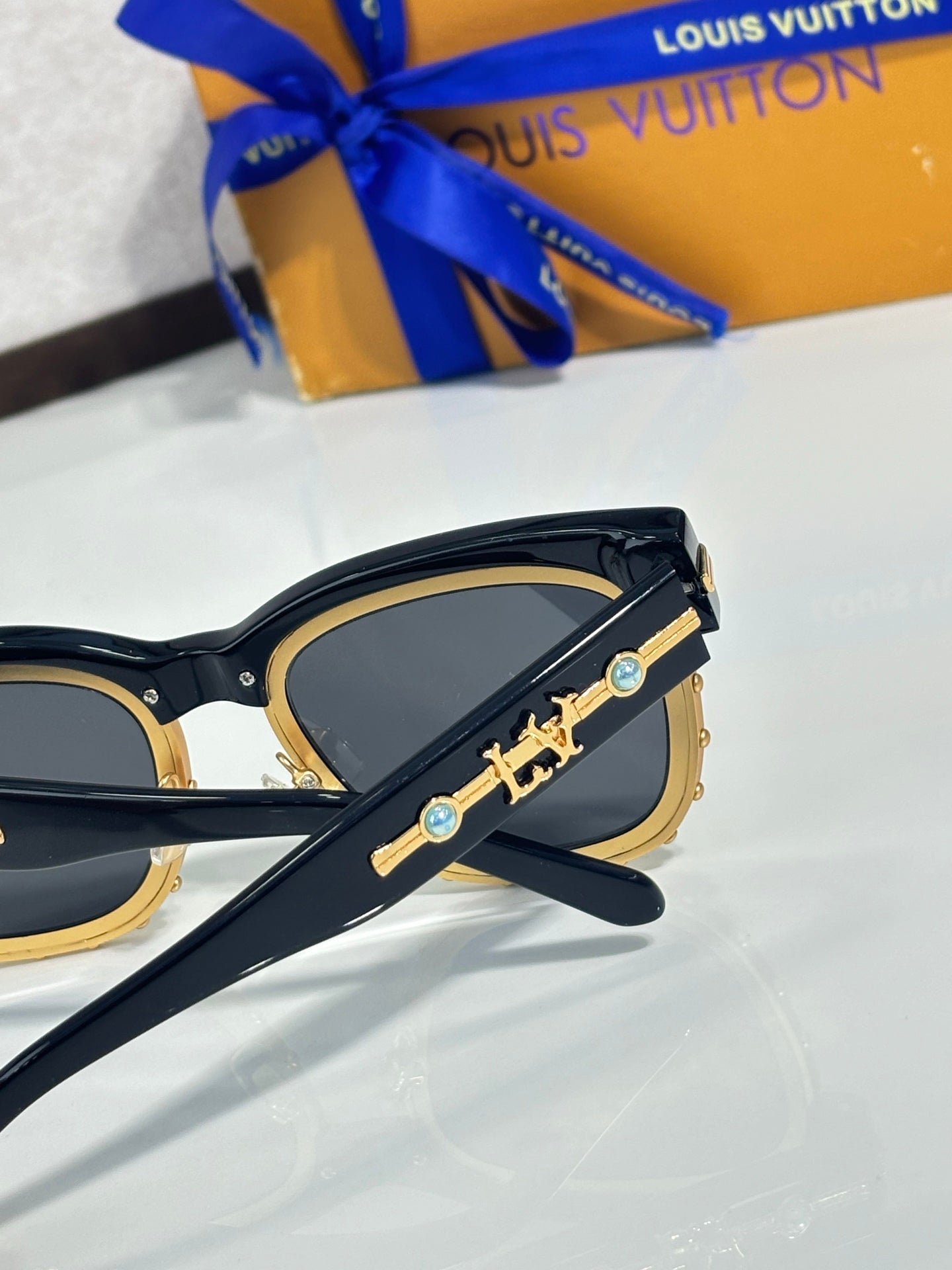 Louis Vuitton sunglasses, side view: gold emblem on black frame, blue-tinted lenses