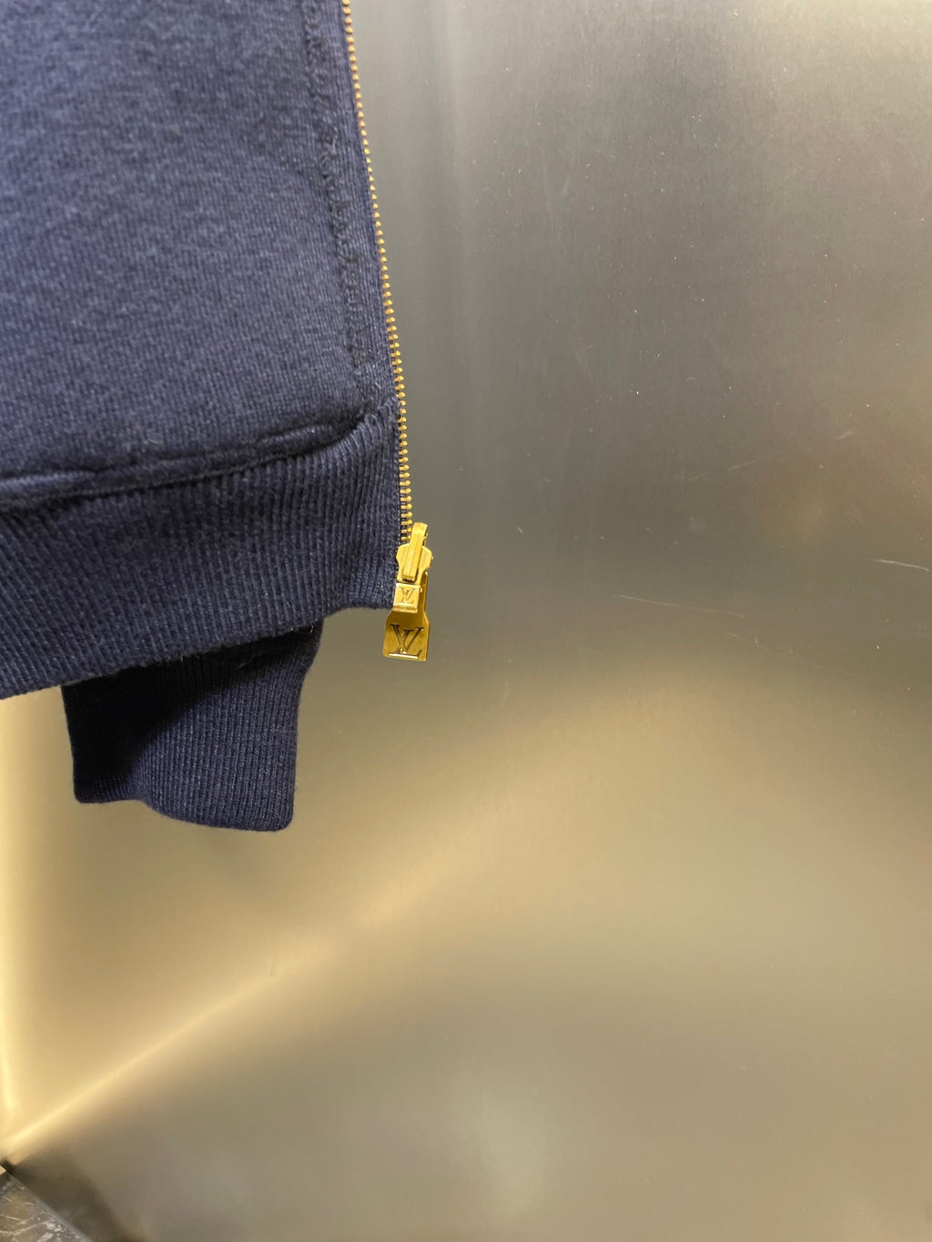 Navy hoodie sleeve cuff with gold zipper pull and small hem vent detail.